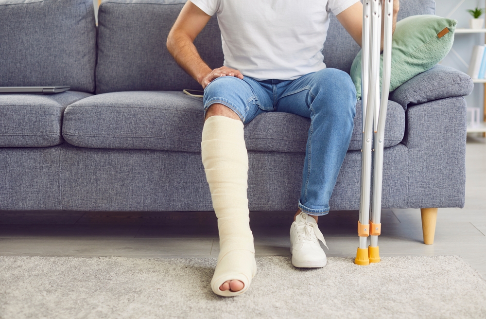 A man with a fractured leg sits on the sofa in his living room, close-up. Concept of injury, bone fracture, home treatment, and rehabilitation.